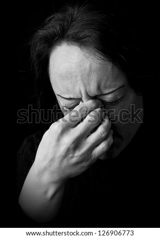 portrait of a woman feeling pain, frowning with hand on head with black background