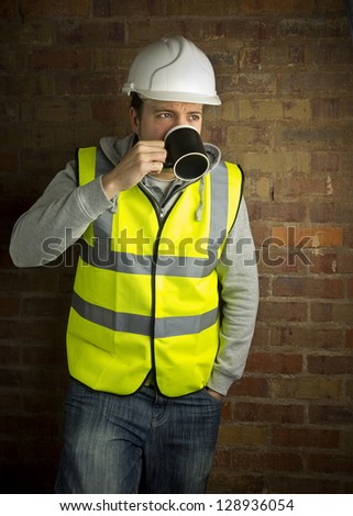 construction worker / builder on coffee break leaning against brick wall