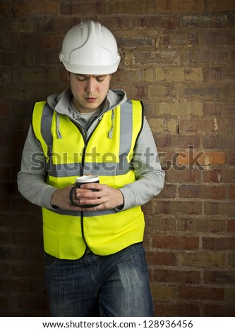 construction worker / builder on coffee break leaning against brick wall looking down