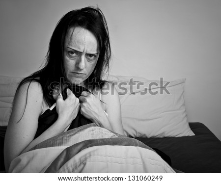 woman covering herself with bed sheets in bedroom looking upset black and white with copy space