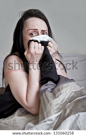 woman under bed sheets in bedroom looking scared