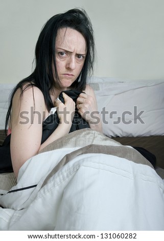 woman covering herself with bed sheets in bedroom looking upset portrait