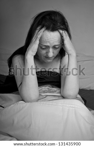woman sitting up in bed with headache, holding head and looking in pain