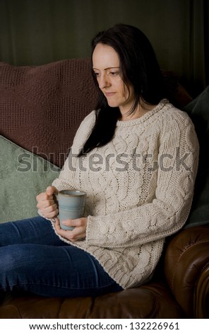 woman thinking while relaxing on sofa with mug of coffee portrait