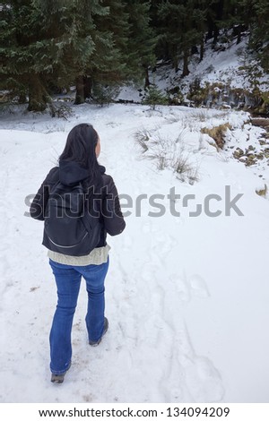 woman hiker walking into forest with thick snow on ground in winter
