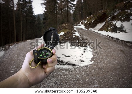 lost man holding compass in middle of forest with two paths to choose from landscape