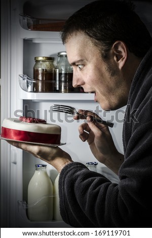 Young happy man eating cake from the fridge