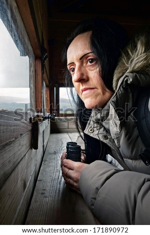birdwatching, a woman with binoculars looking through window in bird hide