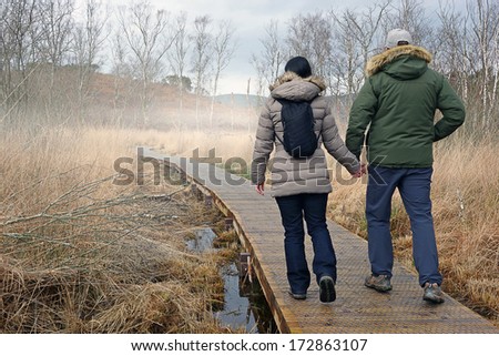 couple holding hands walking along boardwalk on misty morning