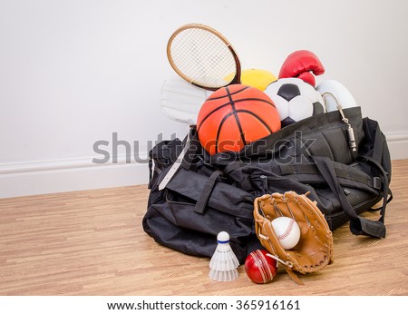 sports equipment in a holdall sports bag on a gym floor. football, rugby, baseball, cricket, basketball, boxing, badminton, squash. with copy space.