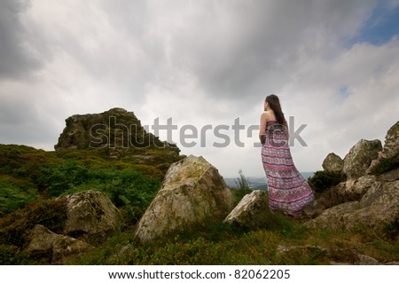 a woman standing in a dress looking up at a rocky mountain
