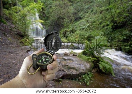 man holding compass near waterfall in jungle