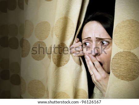 woman shocked at what she sees behind curtains or hiding from intruder