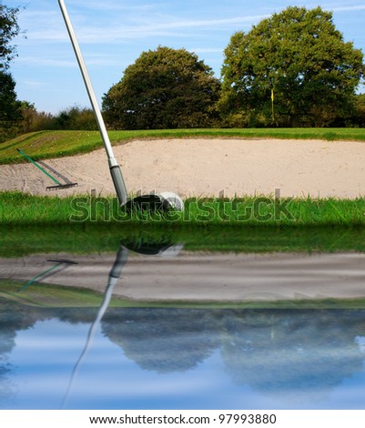 hitting golf ball with club over bunker from water hazard