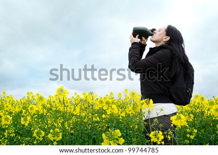 woman drinking from water bottle while standing in field