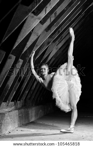 Ballerina wearing white tutu standing on one leg  in hangar