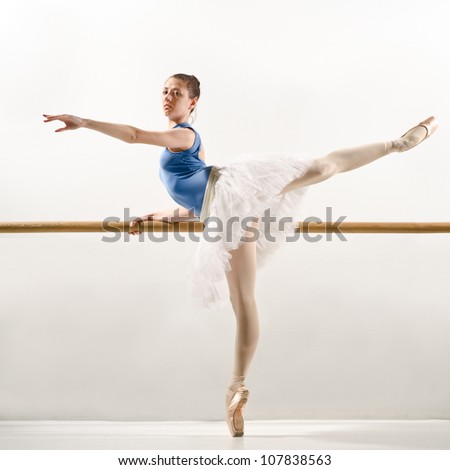 classic ballet dancer in white tutu posing on one leg next to handle bar