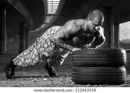 Attractive muscular male body builder doing push-ups outdoor on car tires. Black and white image.