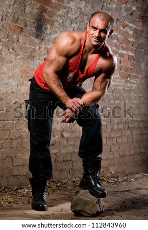 Strong muscular men posing with big rock against old brick wall.