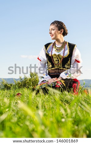 Young female sitting on the grass dressed in traditional Serbian clothing
