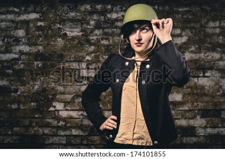 Charming fashion female dressed in army clothes posing against old brick wall.