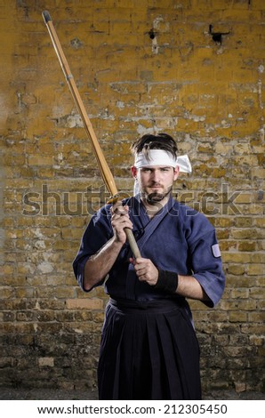 Serious kendo fighter posing against old brick wall