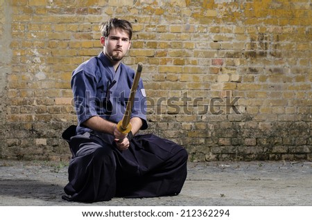 Serious kendo fighter posing against old brick wall.