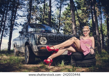 Sexy pin-up girl in short dress sitting and teasing next to retro pickup car
