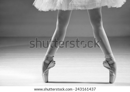 Female ballerina standing on toes in ballet shoes, low section. Grayscale image.