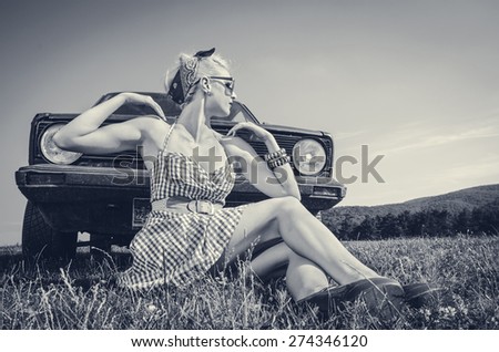 Female pin up style model posing in sexy short dress next to retro car