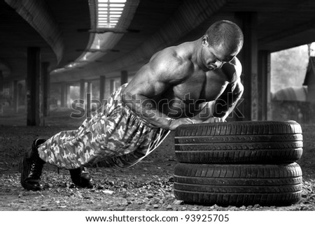 Young body builder doing push-ups outdoor on car tires