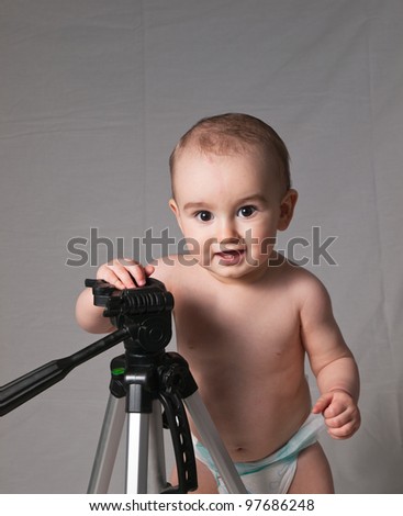 Beautiful baby boy posing in front of gray cloth background holding against a photographic tripod. Used Rembrandt lighting setup with copy space above boy\'s head.