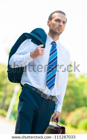 Portrait of business man walking with suit droped over shoulder in park