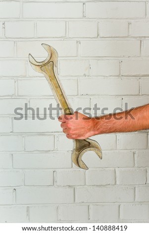 Man\'s hand with big spanner against brick wall