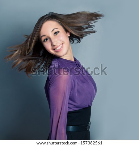 Happy young smiling woman over grey background. Hair fly