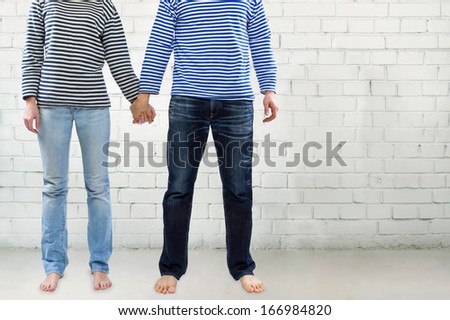 Man and woman holding hands together against white brick wall with copy space. Young couple wearing marine sailor uniform holding hands illustrating love and friendship