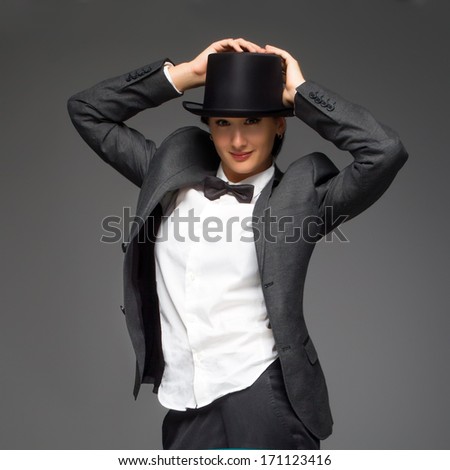 Young  woman wearing top hat over grey background. Woman feels like a man - concept. Retro style young woman against grey background.