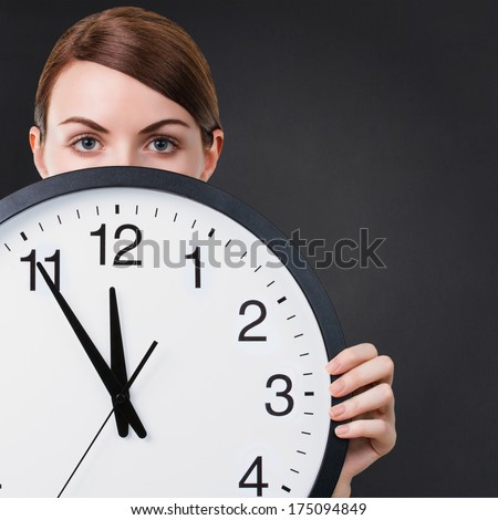 Young woman holding a big clock against back chalkboard background with copy space. Time or business concept