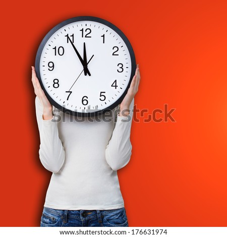 Woman holding a clock over face against orange background. Time concept