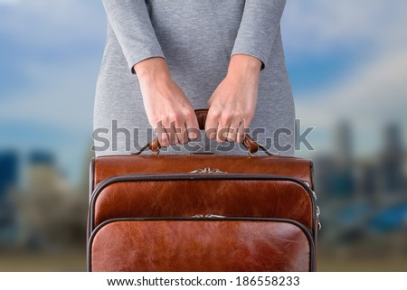 Woman holds leather suitcase in hands against blurred city background