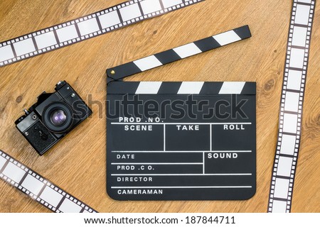 Movie production clapper board, vintage camera and film strips with copy space against wooden background