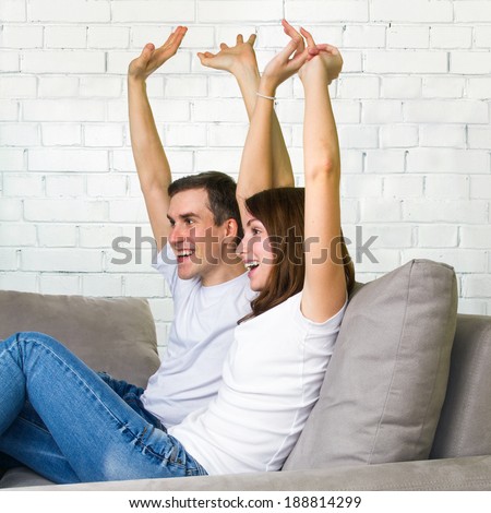 Happy couple with arms raised up. Young couple watching TV on sofa