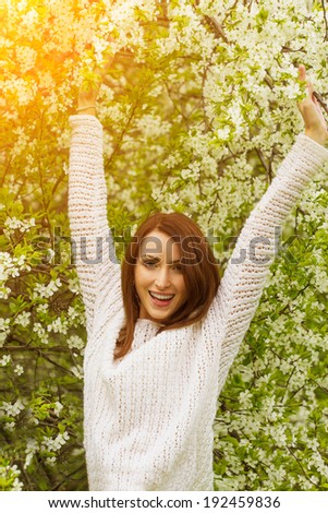 Happy young woman with arms raised up against blossoming spring trees