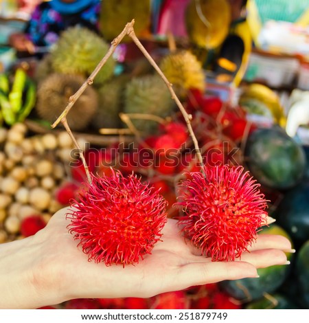 Female hand holding rambutan fruit outdoors at market. Toned effect