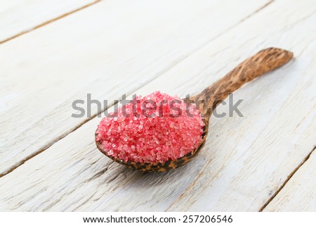 Pink sugar in wooden spoon on white wooden background