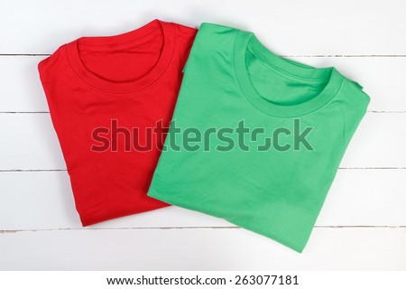 Red and green folded t-shirts on white wooden background. Which is in or out of style?
