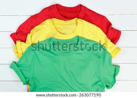 Red, green and yellow t-shirts on white wooden background