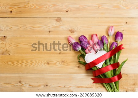 Tulip bouquet with red ribbon and fabric heart on natural wooden texture
