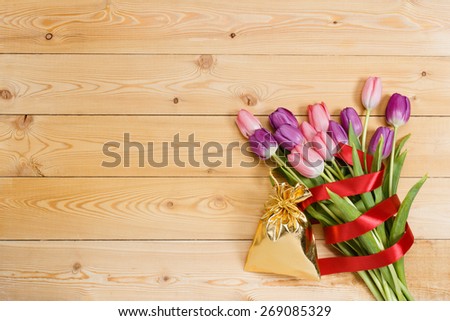 Tulip bouquet with red ribbon and gift in gloden bag on natural wooden texture