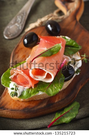 Ham sandwich with olives and chard on an old wooden board.